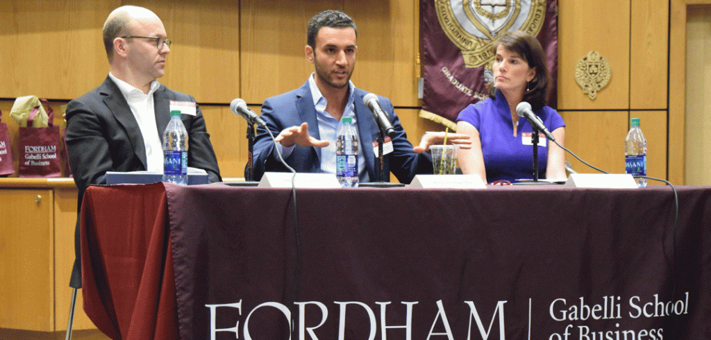 Three panelists discuss Exotic Assets at table with Gabelli School Banner