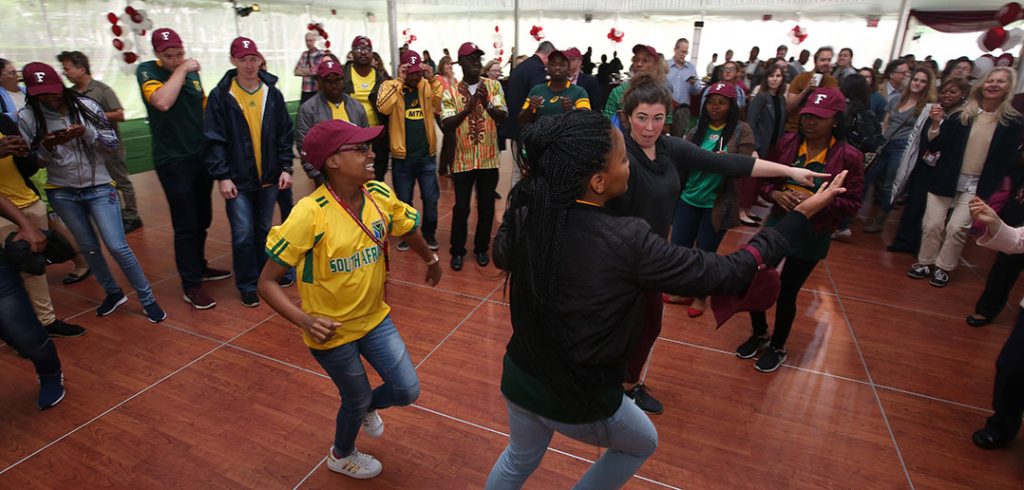 Fordham staff dance with South African exchange students under a tent at Rose Hill.