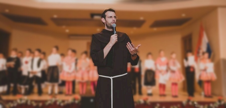 Zeljko Barbaric stands and speaks into a microphone, wearing a Franciscan brown habit.