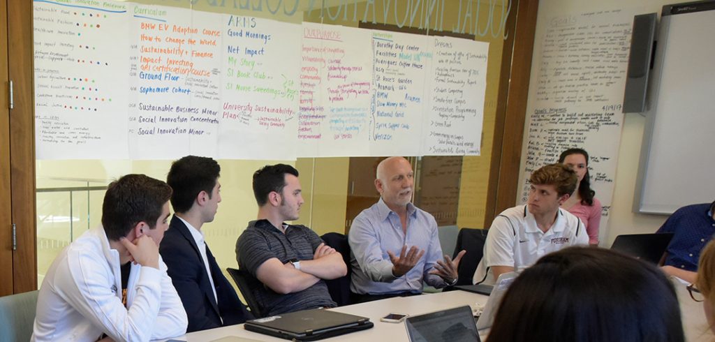 Brent Martini chats with students sitting at a table in the office of the Social Innovation Collaboratory, in Hughes Hall.