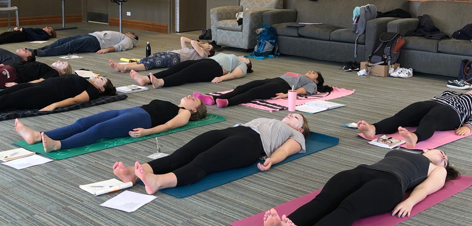 Students lay on yoga mats and towels with their eyes closed and mediate.