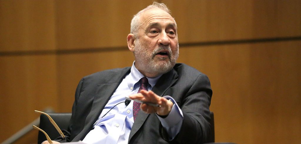 Joseph Stiglitz gestures with his right hand while sitting on stage at the McNally Amphitheatre at Fordham's Lincoln Center campus.