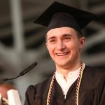 A boy wearing a black graduation gown smiles