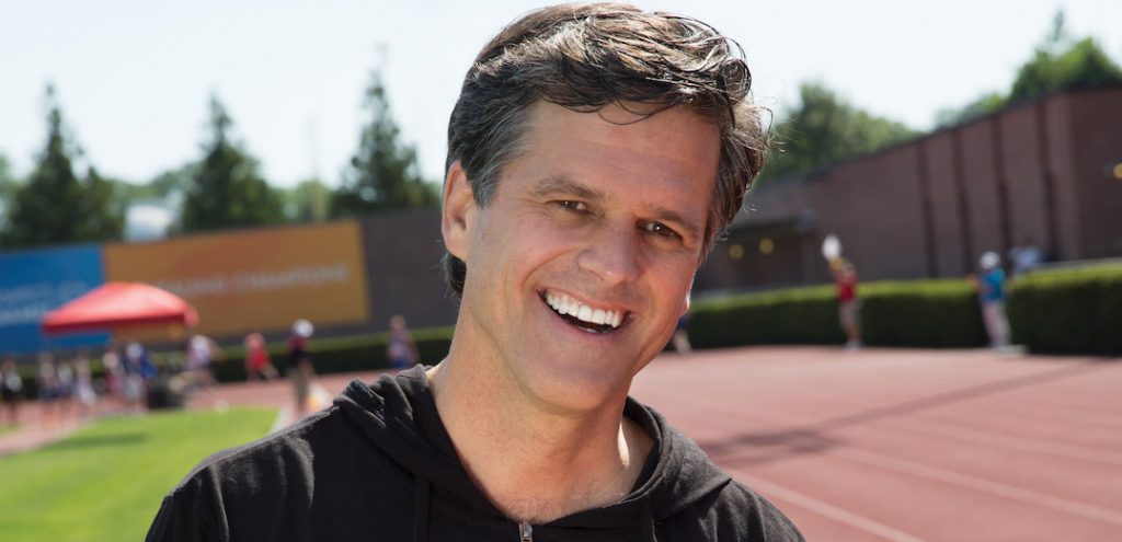 Timothy Shriver, Board Chair of the Special Olympics, in a black hoodie on an athletic track/field