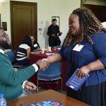 Anthony Abraham Jack shakes hands with a woman while seated at a table