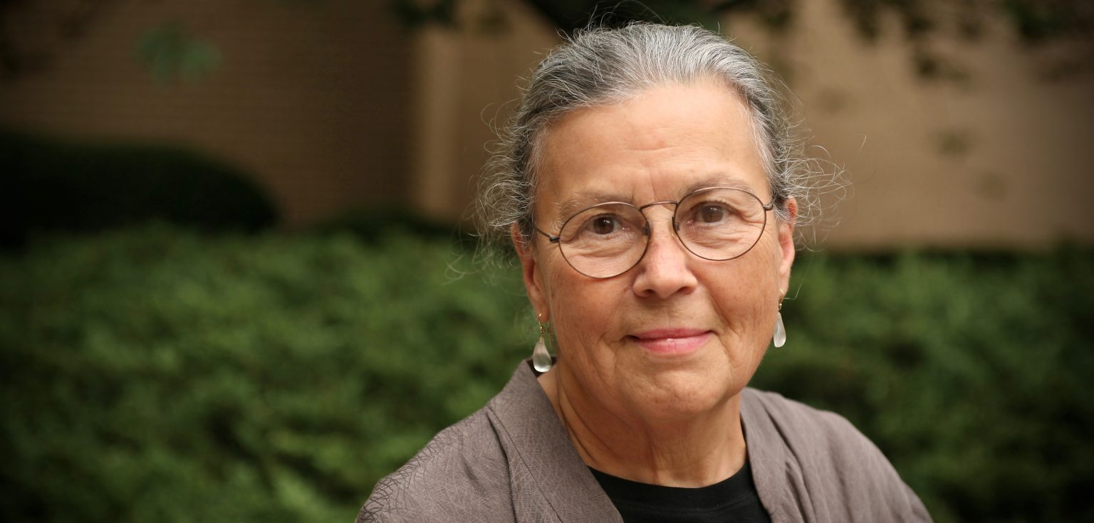 A woman with gray hair and wearing glasses smiles at the camera.