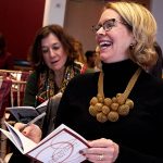 Woman in black sweater with big gold necklace laughing