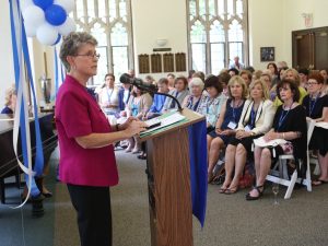 A woman in a pink shirt speaks next to a podium.