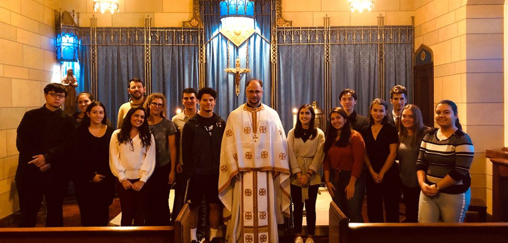 Father Elias Villis, a priest at Christ Our Savior Greek Orthodox Church, stands in the Keating Blue Chapel with students who attended a service there.