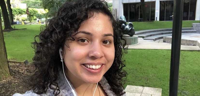 A woman with black curly hair smiles in a selfie.