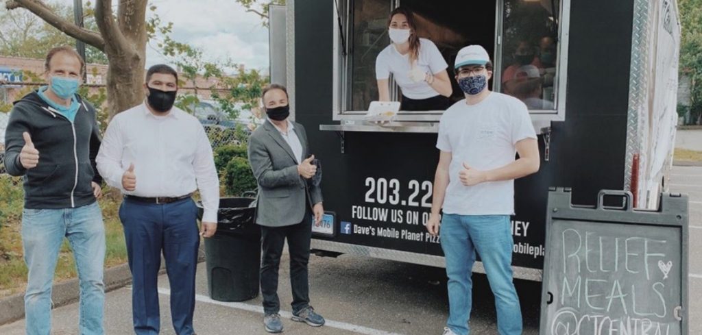 Five people standing by or in a food truck, wearing masks and giving a thumbs-up