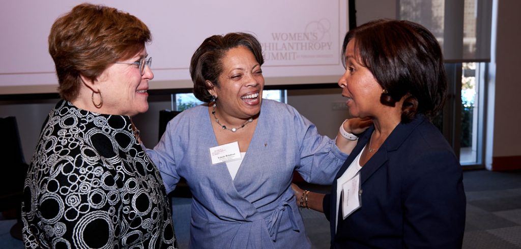 Three women stand next to each other and laugh.