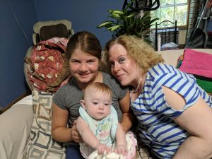 A middle-aged woman smiles next to a girl holding a baby.