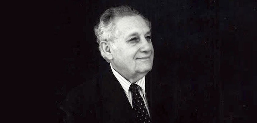 A black and white photo of an elderly man wearing a tie and smiling off into the distance