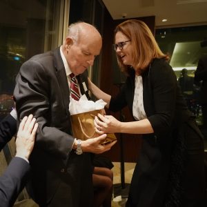 A woman gives an elderly man a gold bag.