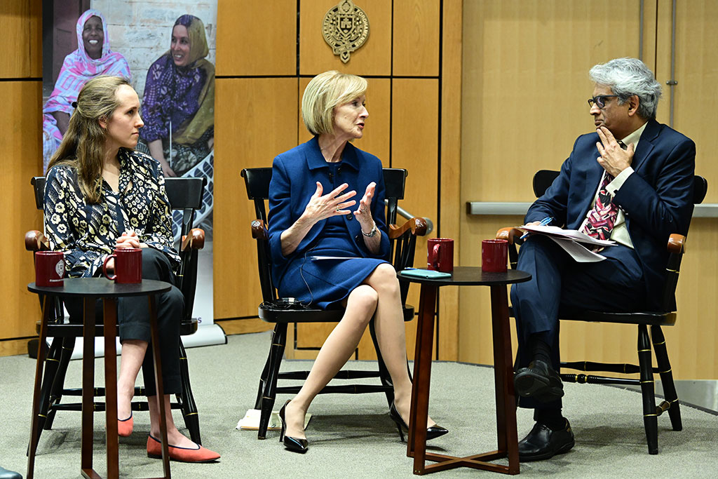 two women seated on stage speaking with a man on stage