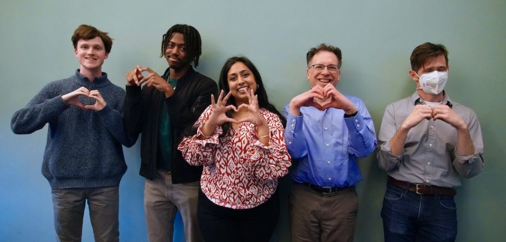 Five people stand together and make a heart shape with their hands.