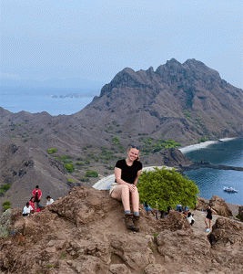 Young woman sitting on a mountain with ocean behind her