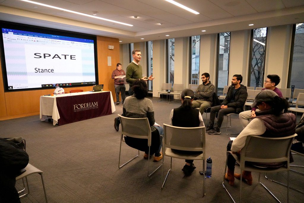 Students seated in a circle listening to a man standing in front of them.