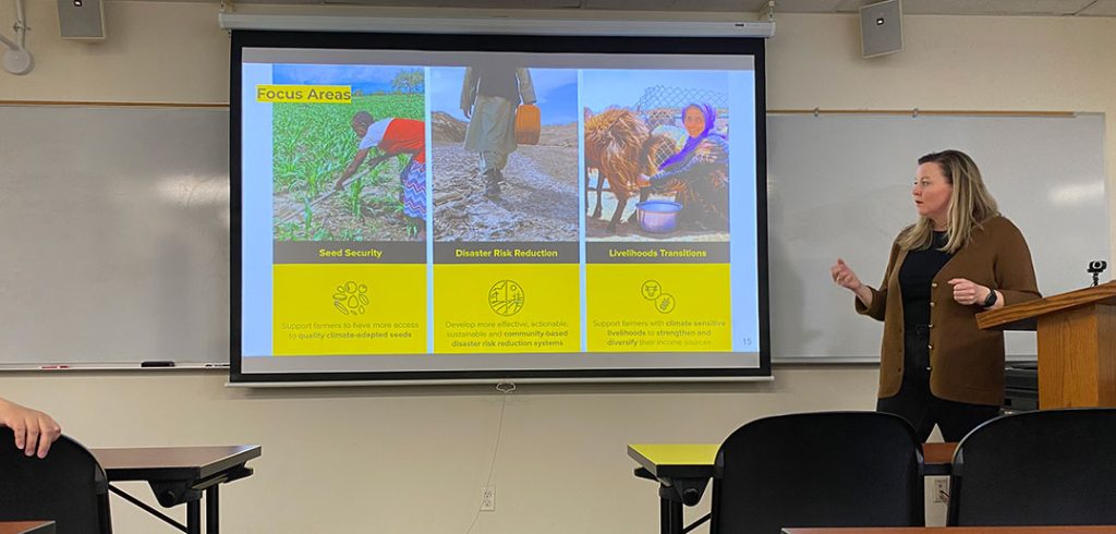 A woman gestures to a powerpoint presentation on a wall.