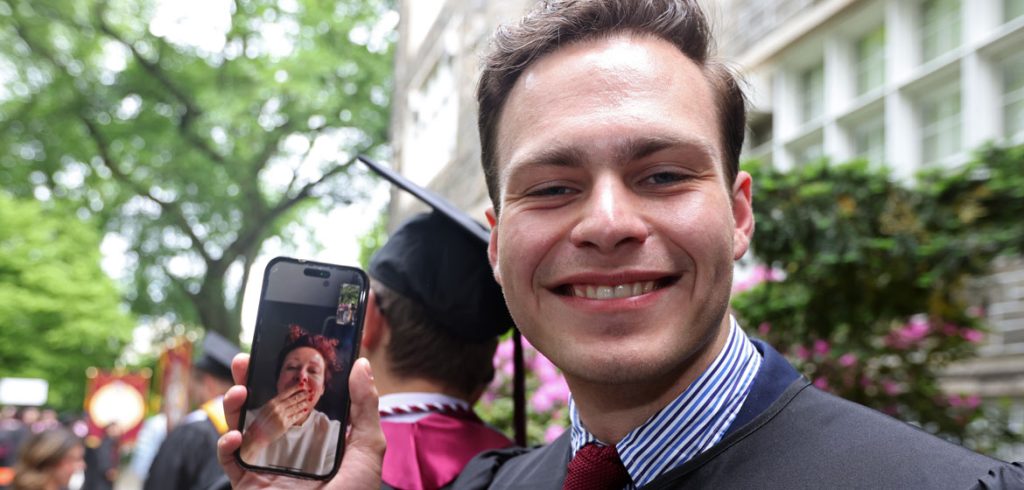 A student holds up a phone showing a video call with his mom