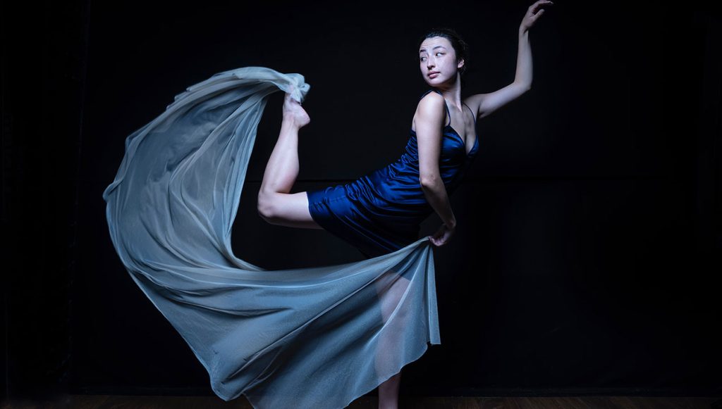 Kathy Liu in a dance pose in front of a black background.