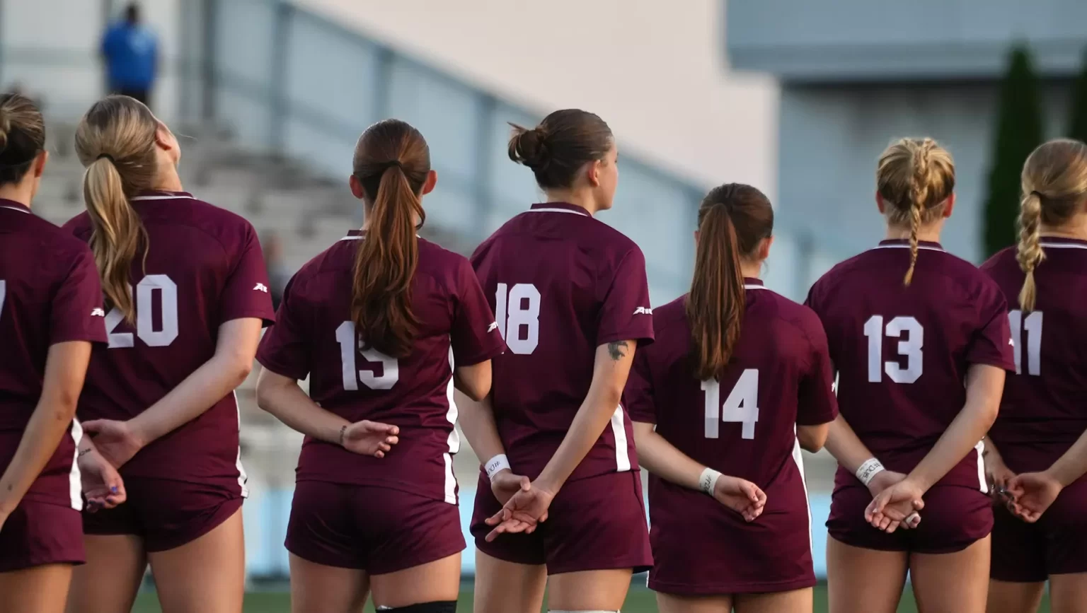 Women's soccer team standing together, showing backs of their jerseys.