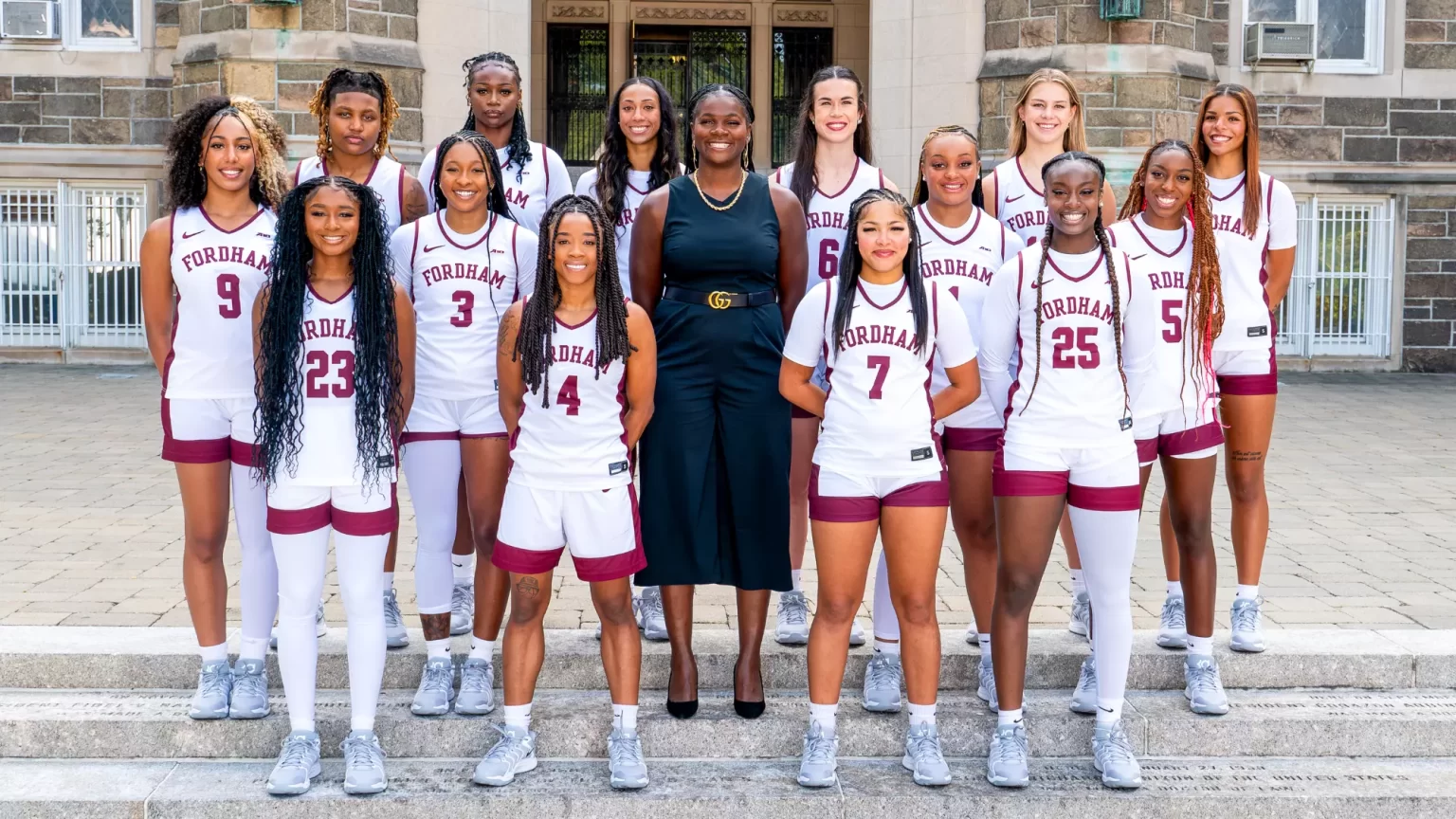 Women's basketball team posing outside of gymnasium with coach.