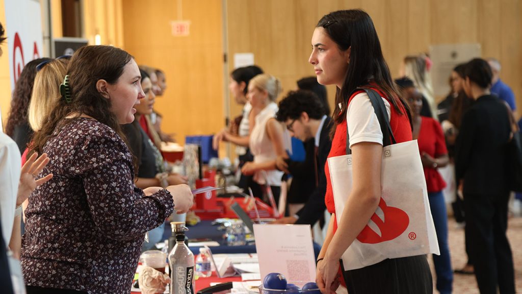 A female student speaks to an older woman standing behind a table.