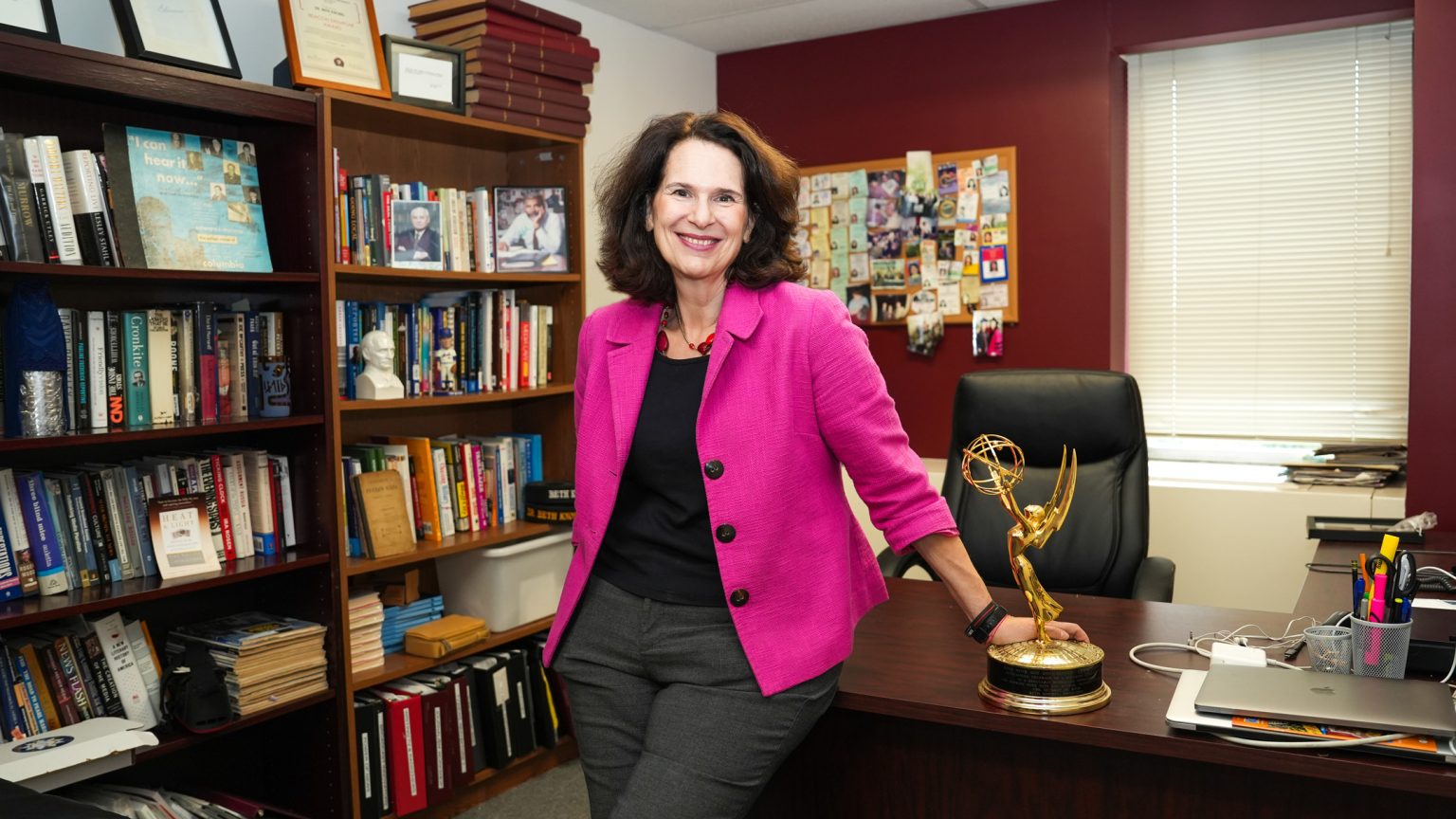 Beth Knobel smiles in front of her office desk with her Emmy.