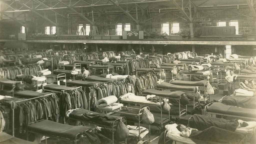 Black and white image shows dozens of cots arrayed on the Rose Hill Gym floor, with a small number of soldiers resting on them