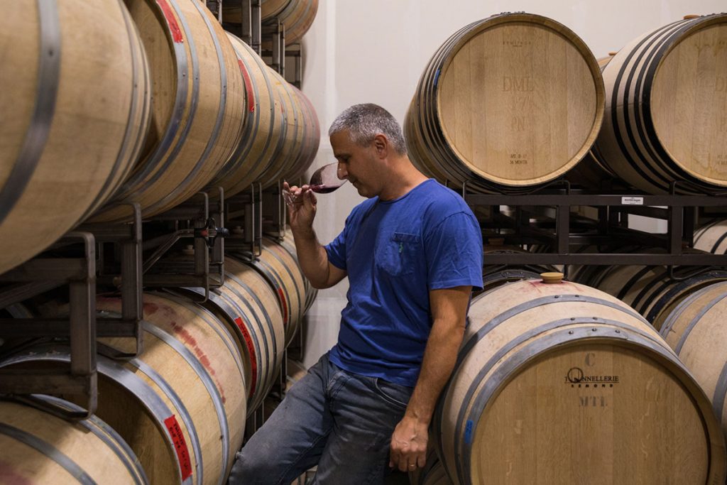 Winemaker Jamie Kutch in profile samples his latest pinot noir amid wine barrels in his winery.