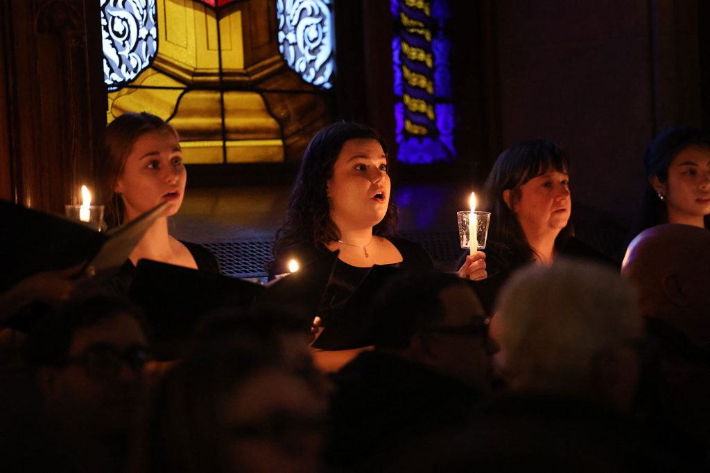 Three members of the choir sing while holding candles.