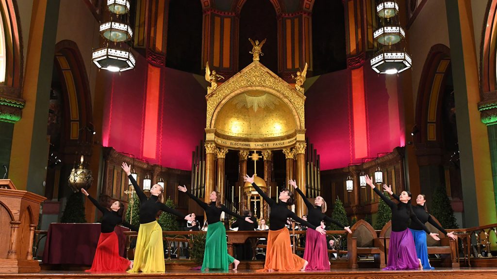 Dancers in colorful outfits stand in front of an altar.