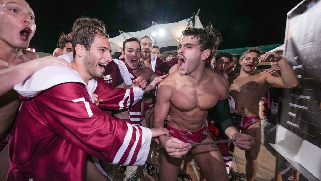 Men's water polo team in uniform, celebrating in group.