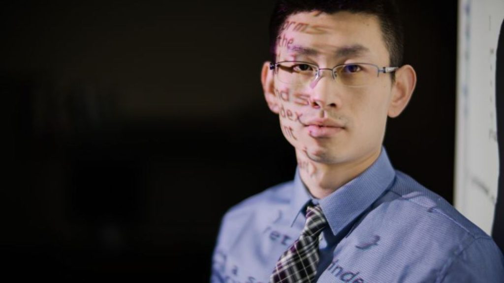 A man stands in front of a white board with words and numbers being projected on to him, representing Fordham's data science master's