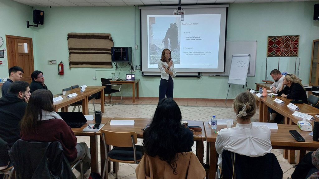 A woman speaks to a group of people seated in a classroom