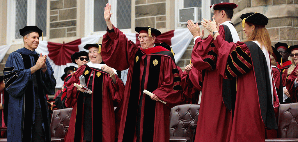 A man in a graduation robe, Father Joseph McShane, accepts an honorary degree at Fordham's commencement ceremony