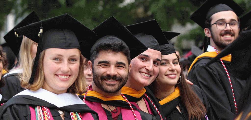 A group of smiling graduates in caps and gowns at Fordham's commencement ceremony