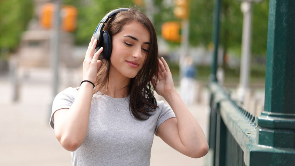 A woman holds onto headphones on her head while her eyes are closed