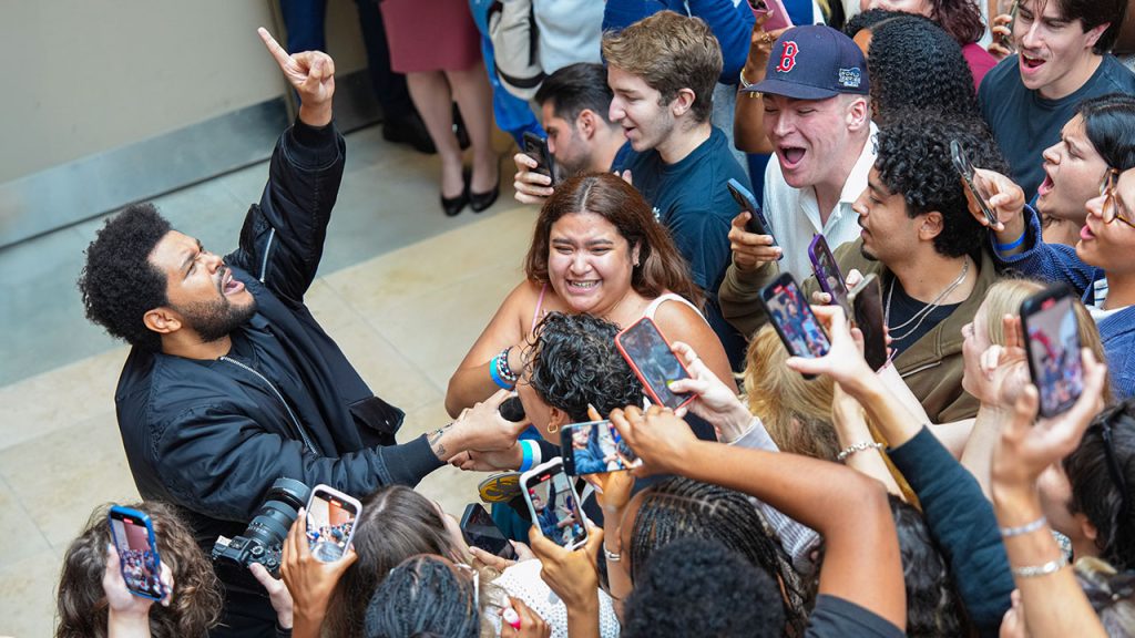 The Weeknd holds a mic out for a student to sing into it
