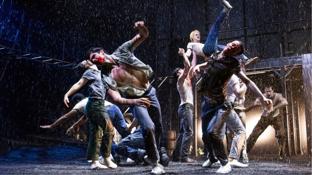 A group of men onstage fighting in the rain during a production of "The Outsiders" on Broadway.
