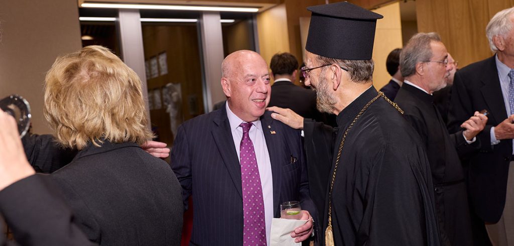 A man in black religious clothes placing his hand on another man's shoulder while greeting him.