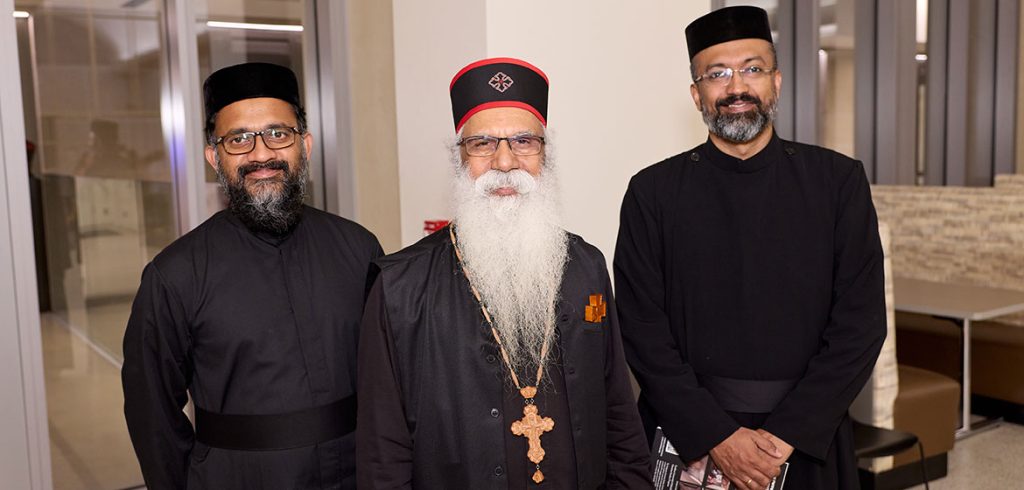 Three men wearing black religious garments smile for the camera.