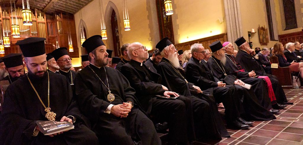 A row of seated men wearing black religious robes looks off to the side.