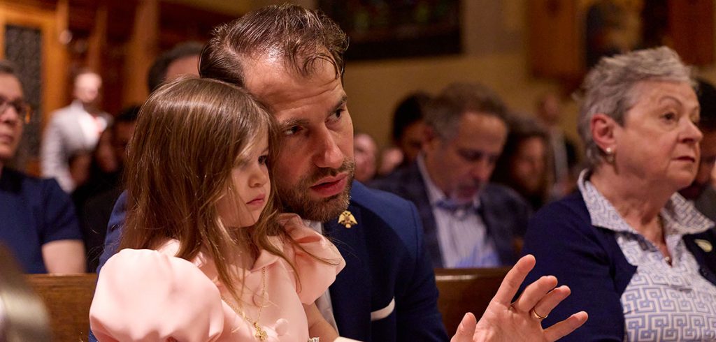 A man with facial hair looks off to the side as a young girl sits in his lap.