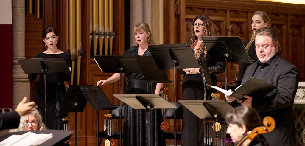 Five members of the Cappella Romana vocal ensemble standing behind lecterns singing together