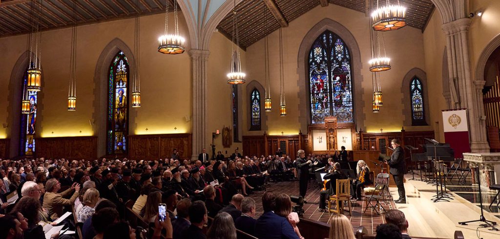 Musicians perform in front of the altar at the University church as people seated listen.