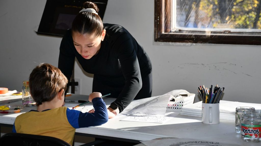 A woman leans over a table assisting a child as he paints, representing Fordham MSW students participating in the Francis Perkins Fellowship