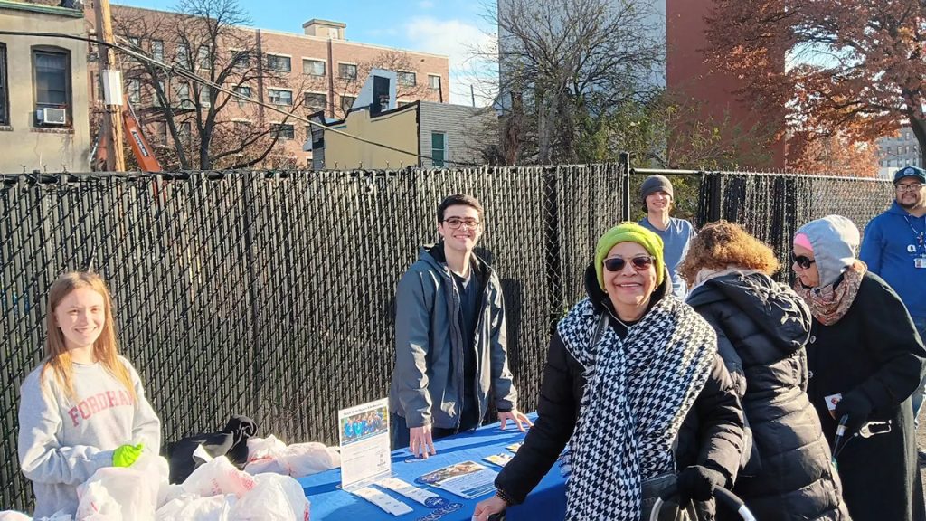 Woman in hat and scarf smiles as she receives food at a turkey giveaway